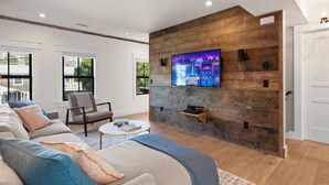 Un salon moderne avec un grand téléviseur à écran plat fixé à un mur en bois, un canapé, un fauteuil et une table basse.