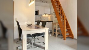 A modern kitchen with white cabinets, a wooden staircase, and a dining area with a table and chairs. - Maisonette Wohnung Meerjungfrau, Dornumersiel (Dornum)