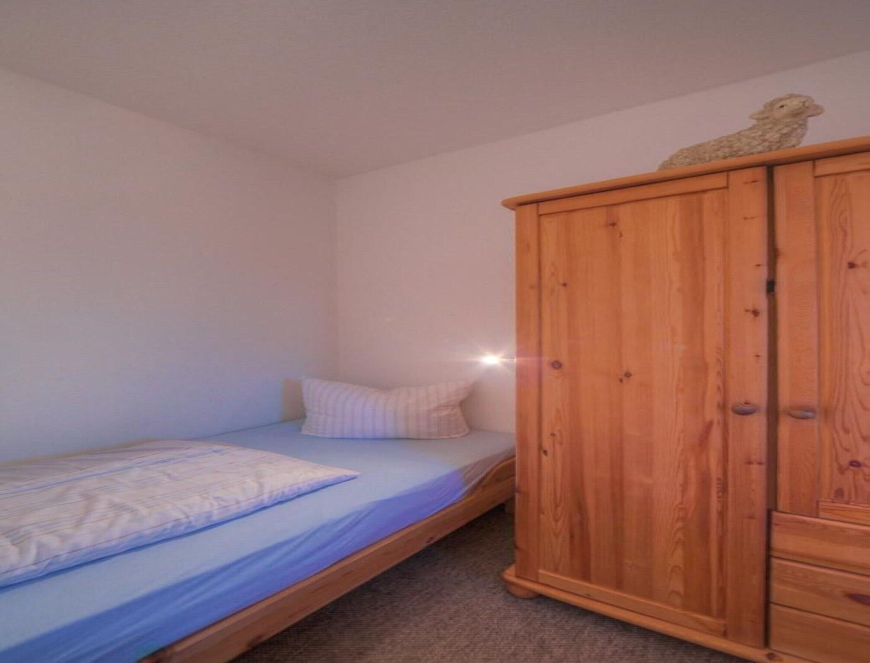Une chambre avec un lit simple, une armoire en bois et un petit objet décoratif posé sur le dessus.
