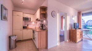 A compact kitchen with modern appliances, a dining area with a TV, and a view of the outside. - Liebevoll Eingerichtetes Appartement (Rechlin)