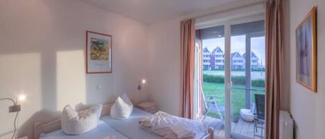 A bedroom with a large bed, a bedside table, a window with curtains, and a view of buildings outside.