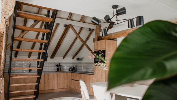 A modern kitchen with exposed wooden beams, a white dining area, and a spiral rug.