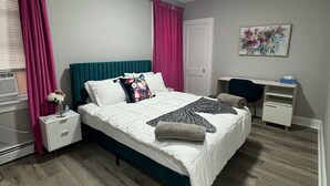 Una camera da letto con un letto, una scrivania, una sedia, un comodino e un quadro appeso al muro.