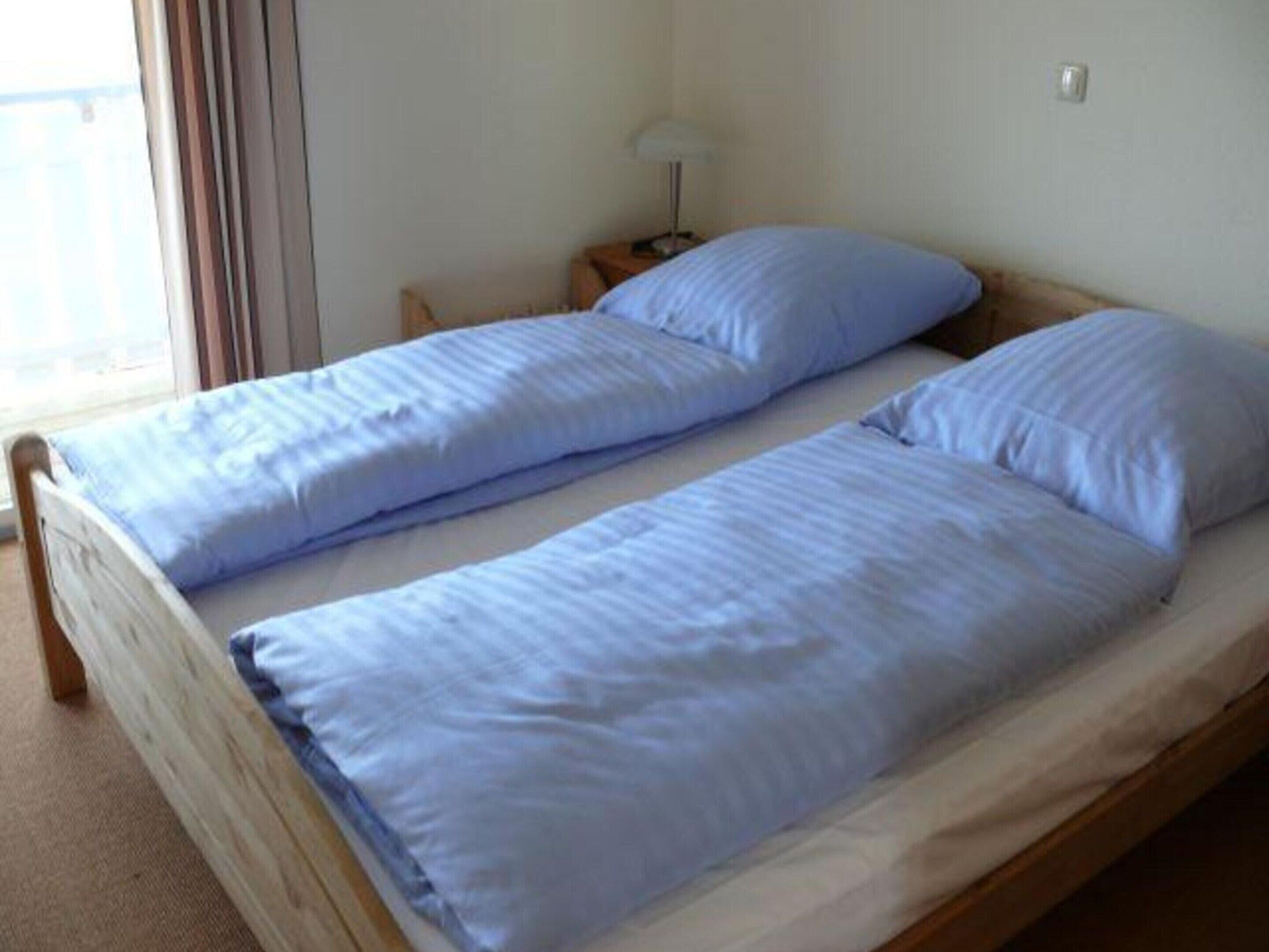 A twin bed with a wooden frame and a single bed with a wooden frame in a room with a window and a nightstand.