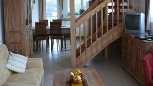 A spacious living area with a wooden staircase, a dining table with chairs, and a television on a wooden cabinet. - Exklusives Appartement in Rechlin (Rechlin)