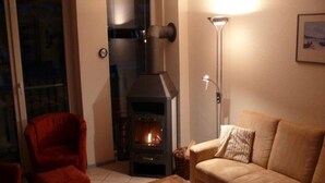 A cozy living room with a fireplace, a red armchair, a beige sofa, and a wooden coffee table. - Exklusives Appartement in Rechlin (Rechlin)