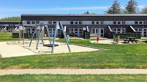 Ein Spielplatz mit Schaukeln und einer Rutsche, einem Picknicktisch und ein Gebäude mit vielen Fenstern im Hintergrund.