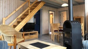 A wooden interior with a staircase, a television on a wooden stand, a black wood stove, and wicker furniture. - Skandinavisches Ferienhaus in Mirow (Mirow)