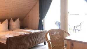 A cozy room with a wooden ceiling, a bed with pillows, a wicker chair, and a table. - Skandinavisches Ferienhaus in Mirow (Mirow)