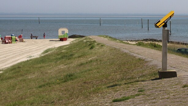 Ein Strand mit einem kleinen Gebäude, einem Weg und einem Wegweiser.