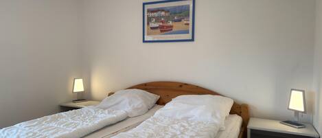 A double bed with white bedding, a wooden headboard, two bedside tables with lamps, and a framed picture of boats on the wall.
