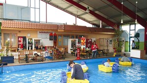 Una piscina coperta con diverse corsie, una zona relax con tavoli e sedie, e un edificio con tetto rosso e insegne.