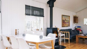 A cozy living room with a fireplace, white walls, and a dining area with white chairs.