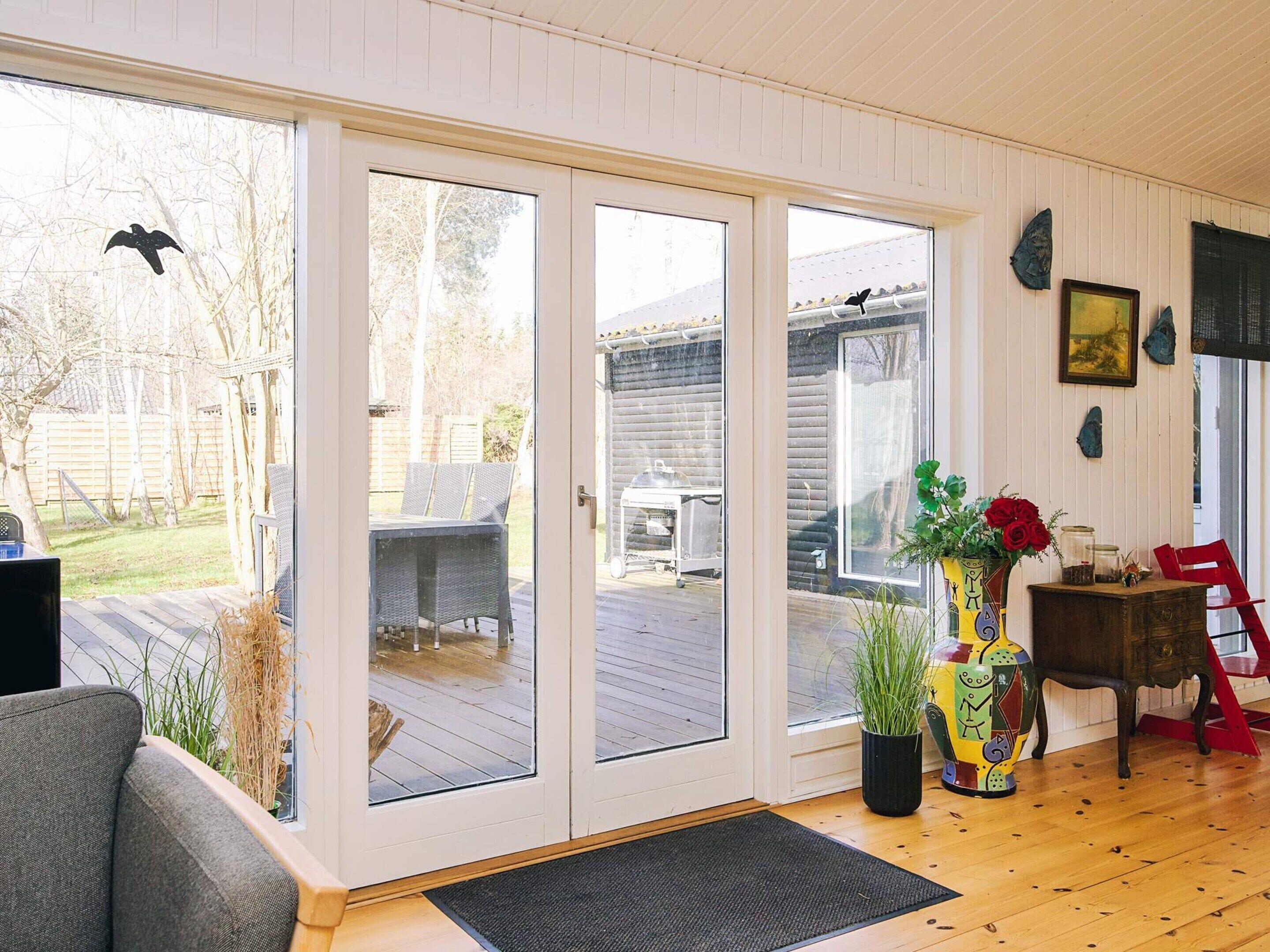 A room with a sliding glass door leading to an outdoor deck, a black chair, a colorful vase with flowers, and a wooden table.