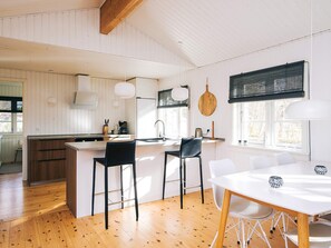 Una cocina moderna con una isla central, taburetes negros, una mesa de comedor blanca y un amplio ventanal con vistas.