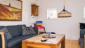 A living room with a sofa, a wooden coffee table, a painting of a landscape, a cabinet, and a window.