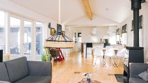 A spacious living area with a high ceiling, a dining area with white chairs, and a kitchen with a black stove. - 6 Person Holiday Home in Grevinge (Grevinge)