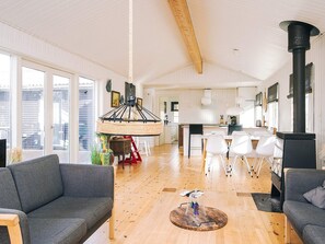 Un amplio espacio de sala de estar con techo alto, un comedor con sillas blancas y una cocina con estufa negra.