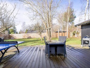 Une terrasse en bois avec une table de ping-pong, des sièges d’extérieur et un barbecue.