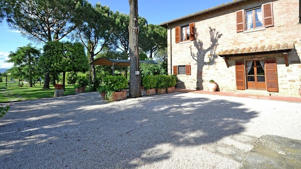 Un bâtiment en pierre avec une allée de gravier et un grand arbre au premier plan.