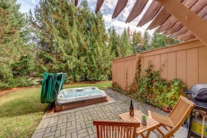 Eine Terrasse mit Whirlpool, Holzstühlen und Grill.