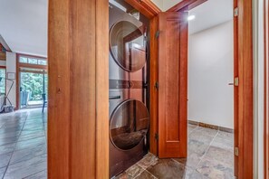 A wooden door with two circular windows, leading to a room with a tiled floor and a view of the outdoors.