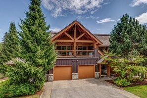 A two-story log cabin with a garage, surrounded by evergreen trees. - 3BD/3BA Townhome Hot Tub, Garage (Whistler)