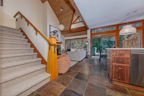 Eine Treppe mit Holzgeländern, ein Wohnbereich mit einer Couch und einem Couchtisch sowie eine Küche mit Holzschränken und einem Edelstahlkühlschrank.