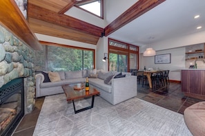 A spacious living area with a stone fireplace, a grey sofa, a wooden coffee table, and a dining area with a wooden table and chairs.
