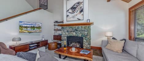 A living room with a stone fireplace, a sofa, a coffee table, and a bookshelf.