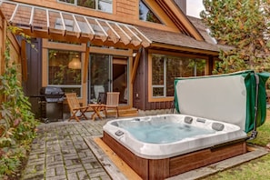 Ein Whirlpool in einem Garten mit einer Holzterrasse, einem Grill und zwei Stühlen.