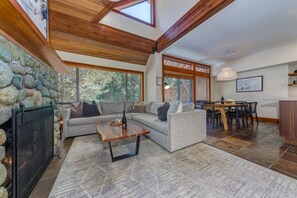 Ein Wohnzimmer mit Kamin aus Stein, einer Couch, einem Couchtisch und einem Essbereich mit Tisch und Stühlen.