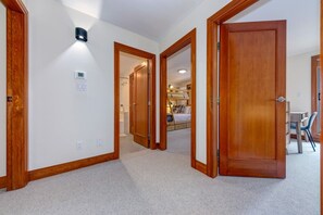 A hallway with wooden doors, carpeted flooring, and a visible bathroom with a shower and toilet.