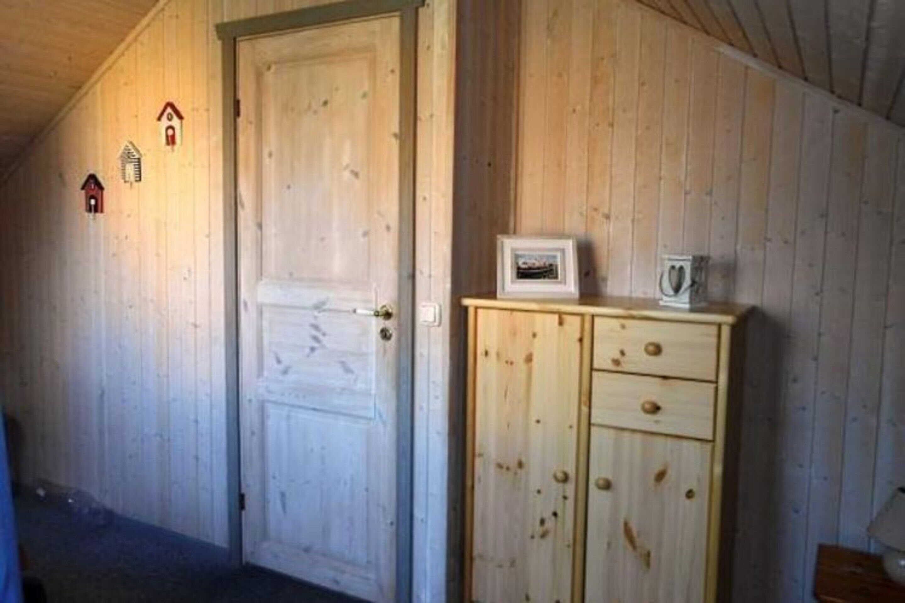 A wooden interior with a closed door, a cabinet with a picture frame, and small house-shaped decorations on the wall.
