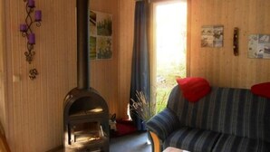 A cozy living room with a fireplace, a striped sofa, and a window with curtains. - Ferienhaus im Ferienpark Mirow (Mirow)