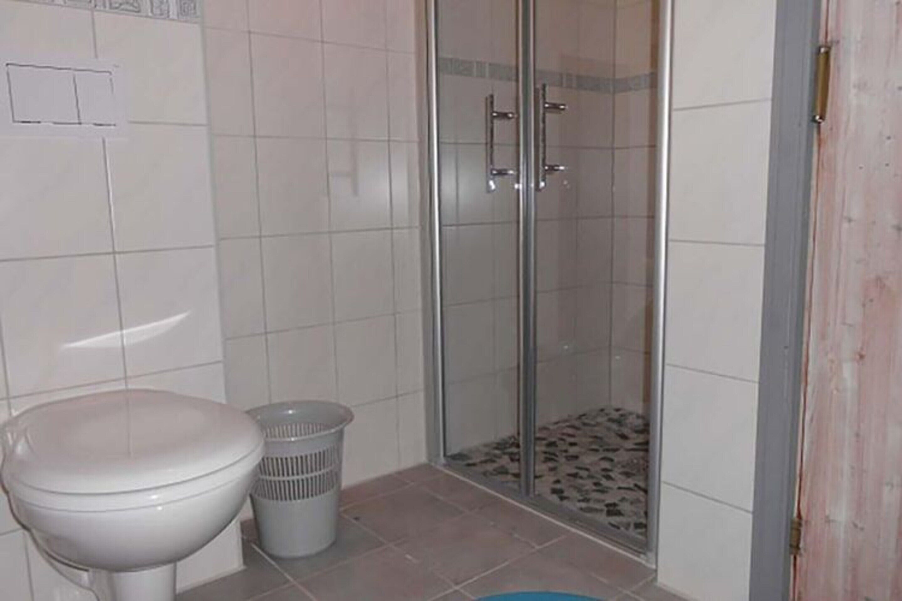 Une salle de bain avec des toilettes, une douche dotée de parois en verre et un sol carrelé.