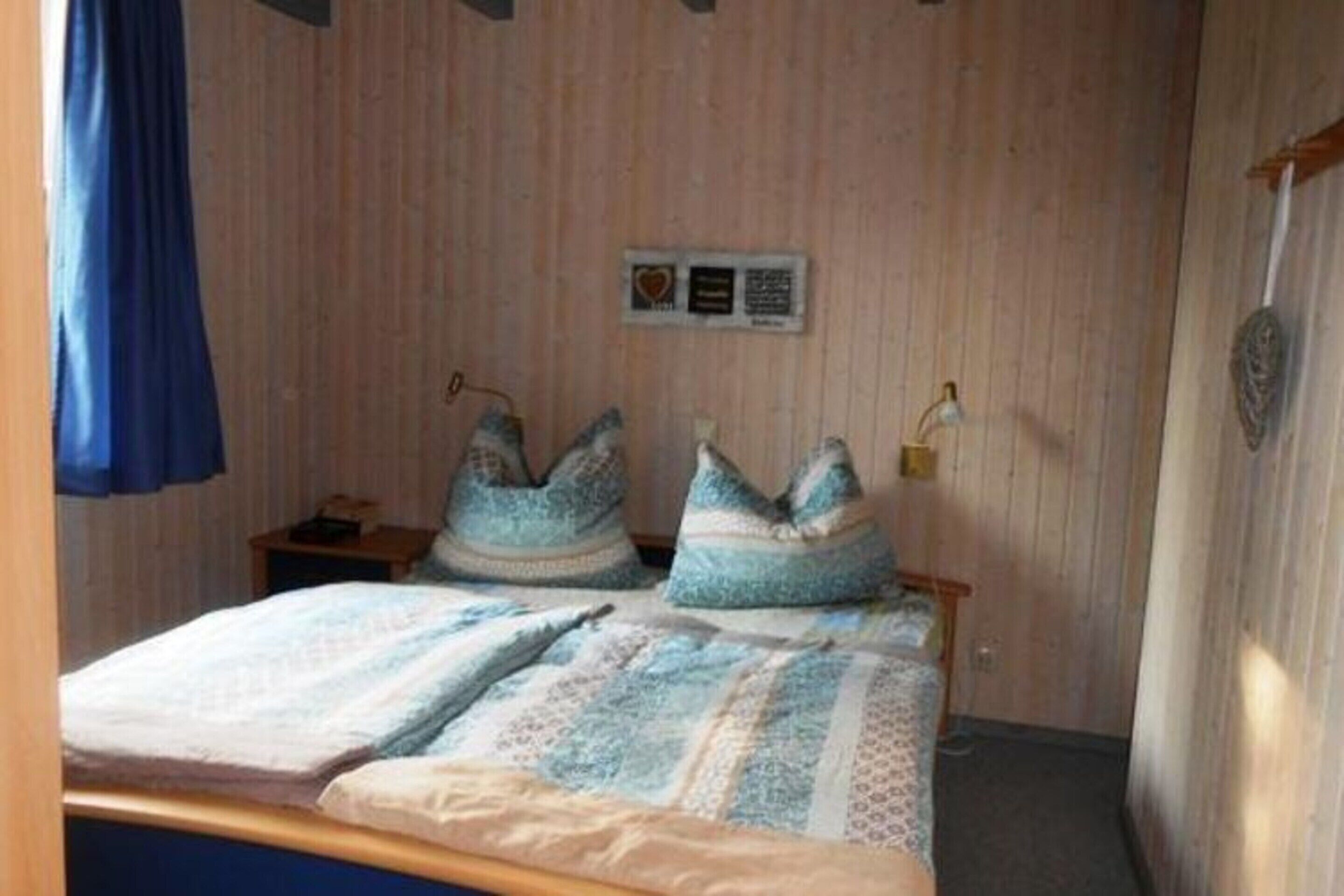 A bedroom with a wooden wall, a bed with patterned bedding, and two pillows.