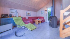 A cozy room with a green lounge chair, red sofa, and a small table. There is a heater, a fireplace, and a window with a view. - Ferienhaus im Skandinavischen Stil (Mirow)