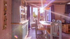A dining area with a table and chairs, a wooden cabinet, and a window with curtains. - Ferienhaus im Skandinavischen Stil (Mirow)