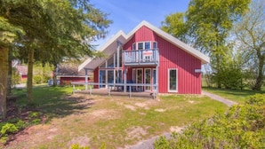 A red two-story house with a balcony, surrounded by trees and a grassy yard. - Ferienhaus im Ferienpark Mirow (Mirow)