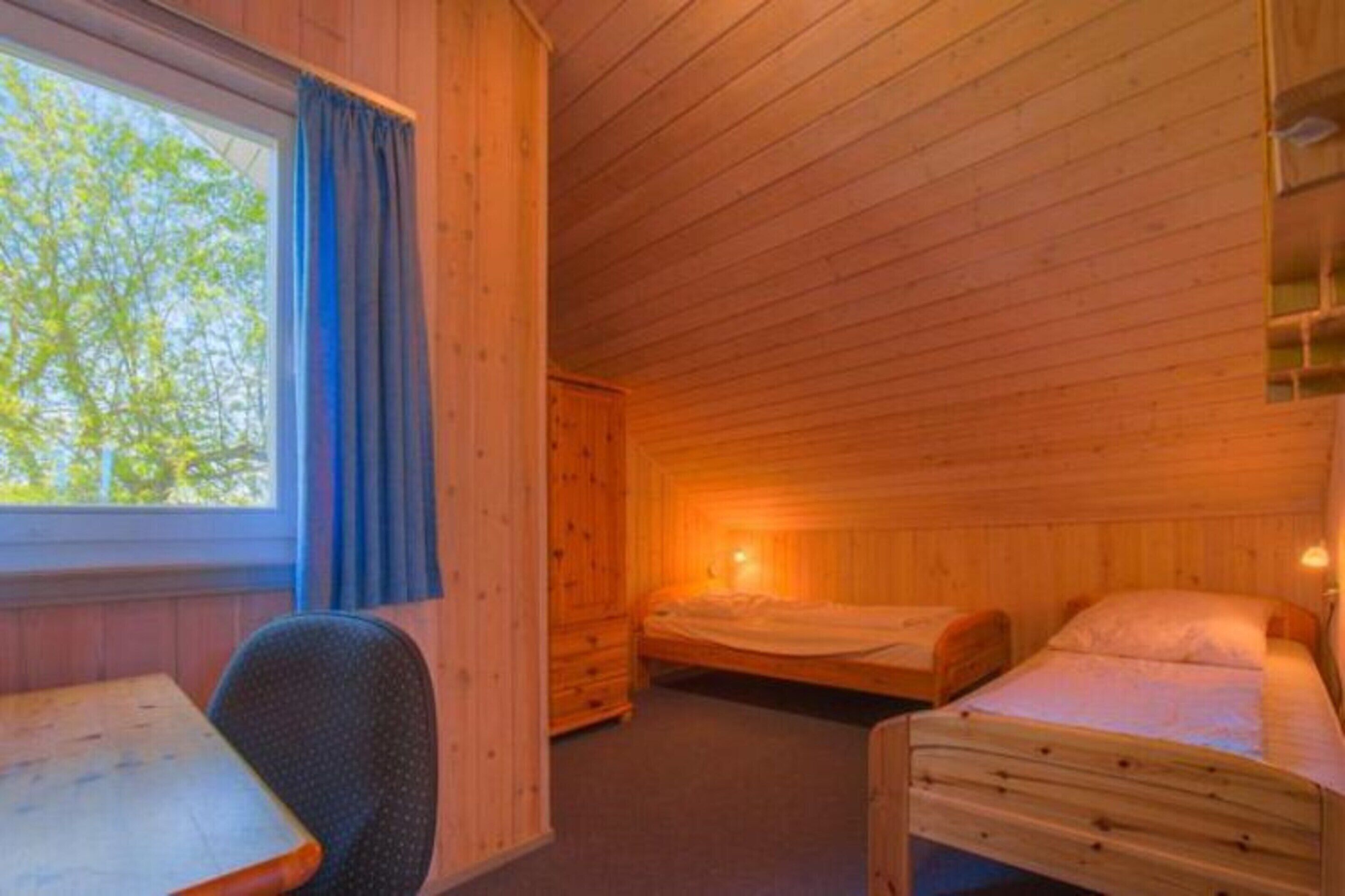 A wooden cabin room with a single bed, a desk, and a chair.