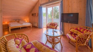 A cozy room with a bed, two wicker chairs, a glass table, and a TV. - Ferienhaus im Ferienpark Mirow (Mirow)