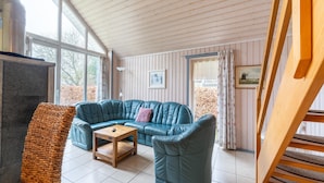 Un salon chaleureux avec un canapé d’angle, une petite table en bois et un pouf en fibres tressées.
