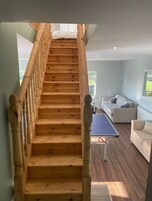 Uma escada de madeira leva a um quarto com cama e vista para o exterior.