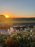 Terraço no telhado com mesa e cadeiras, rodeado por vasos de plantas e flores.