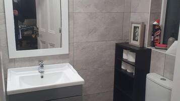 A bathroom with a white sink, a mirror, a toilet, and a shelf with toiletries.