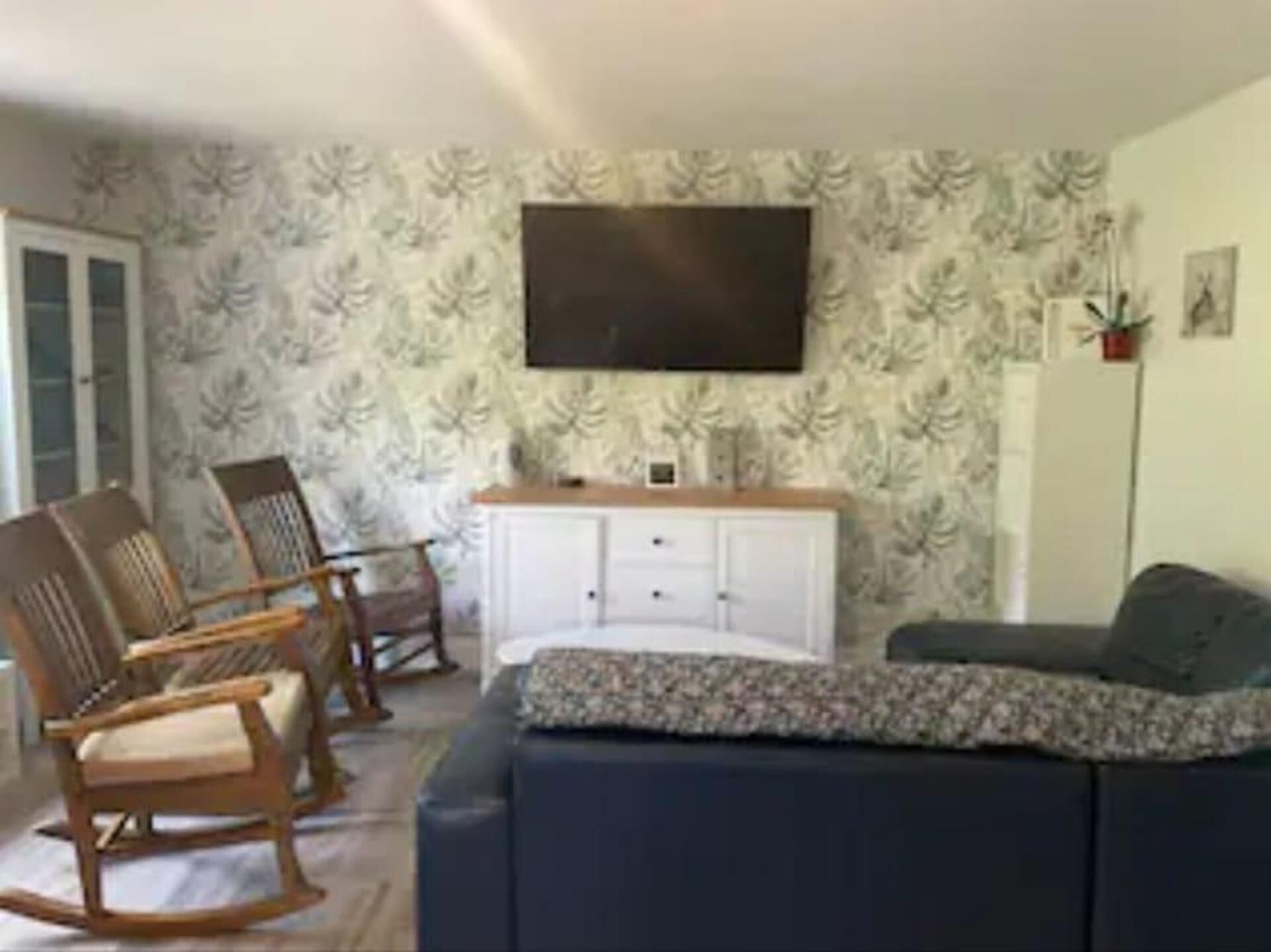 Ein Wohnzimmer mit einer Couch, zwei Schaukelstühlen, einem weißen Schrank und einem an der Wand befestigten Flachbildfernseher.