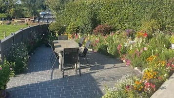 Une terrasse dallée, agrémentée d’une table et de chaises, et entourée d’une variété de fleurs et de plantes aux couleurs vives.