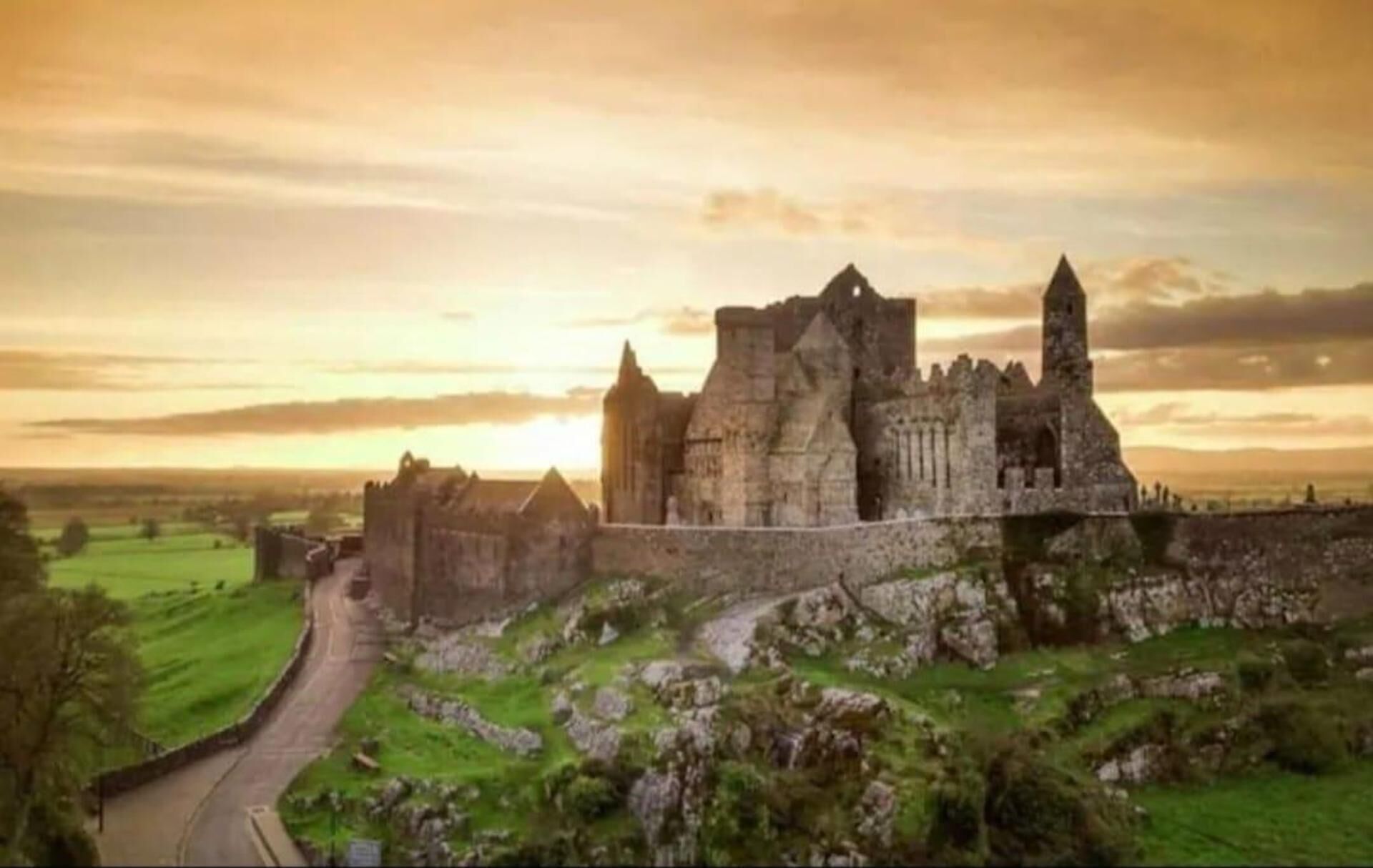 A historic castle with a prominent tower, surrounded by green fields and a winding road.