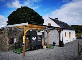 Um edifício rústico chamado "The Coffee Coop", com fachada de pedra, varanda de madeira e uma placa.